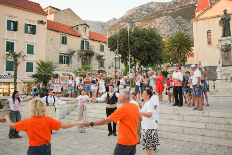 Izvedba narodnog plesa na otvorenom trgu pred mnogobrojnom publikom i starim kamenim kućama.